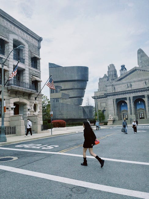 A woman crosses the street with modern architectural buildings in the background, American flags visible.